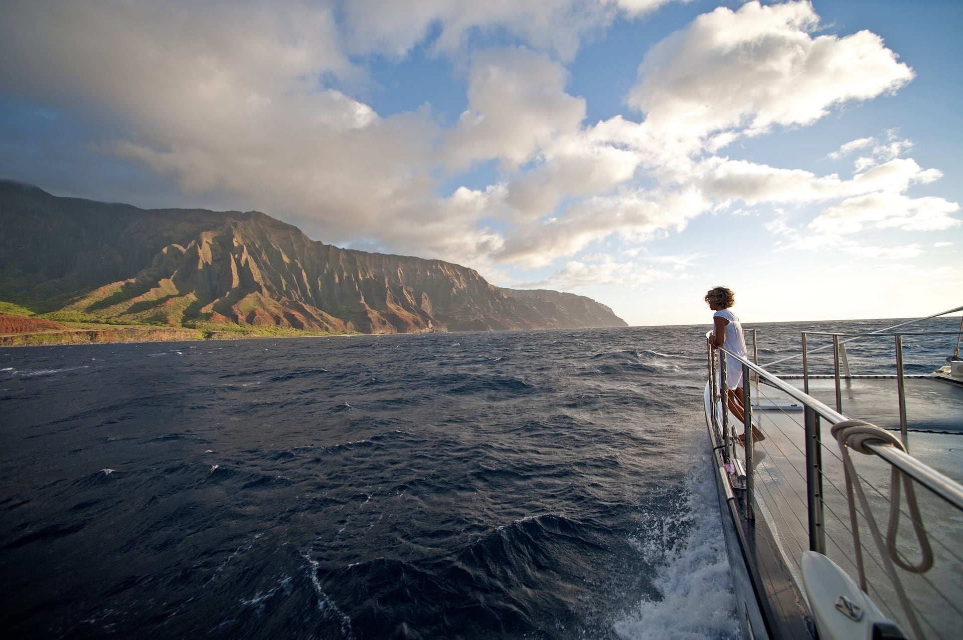 Person standing on the deck of Captain Andy's yacht, admiring the Na Pali Coast at sunset