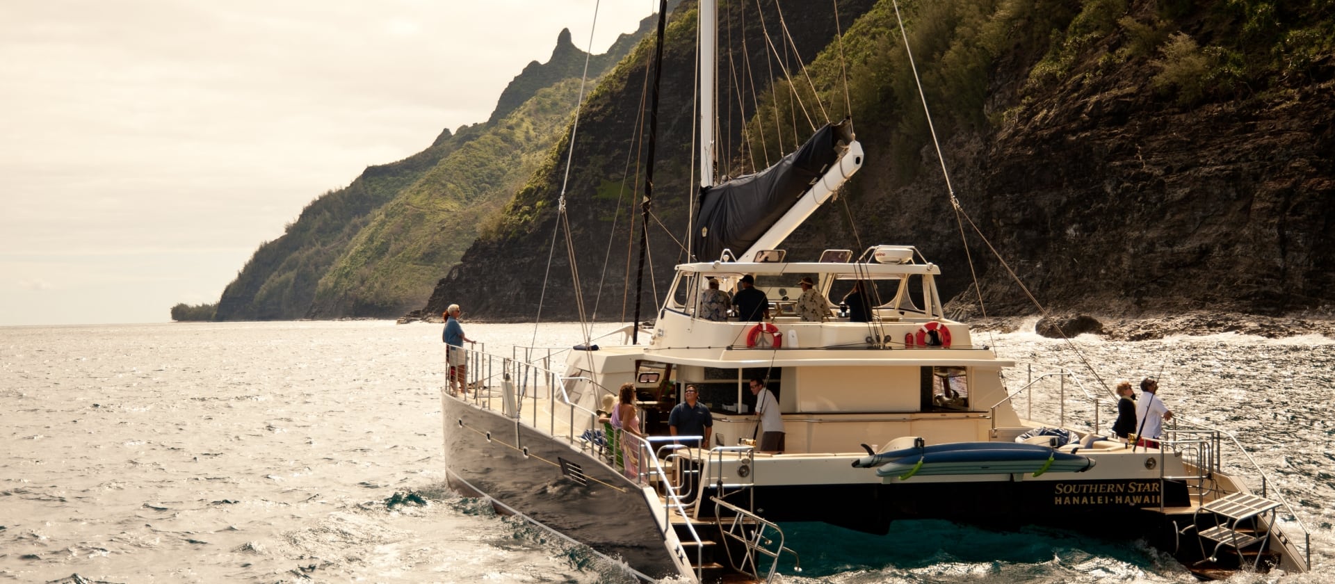 Captain Andy's catamaran, Southern Star, sailing along the Na Pali Coast with lush green cliffs in the background and passengers enjoying the view