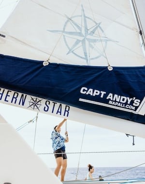 Crew member adjusting the sail on Captain Andy's catamaran, Southern Star, with the boat's name and logo visible.