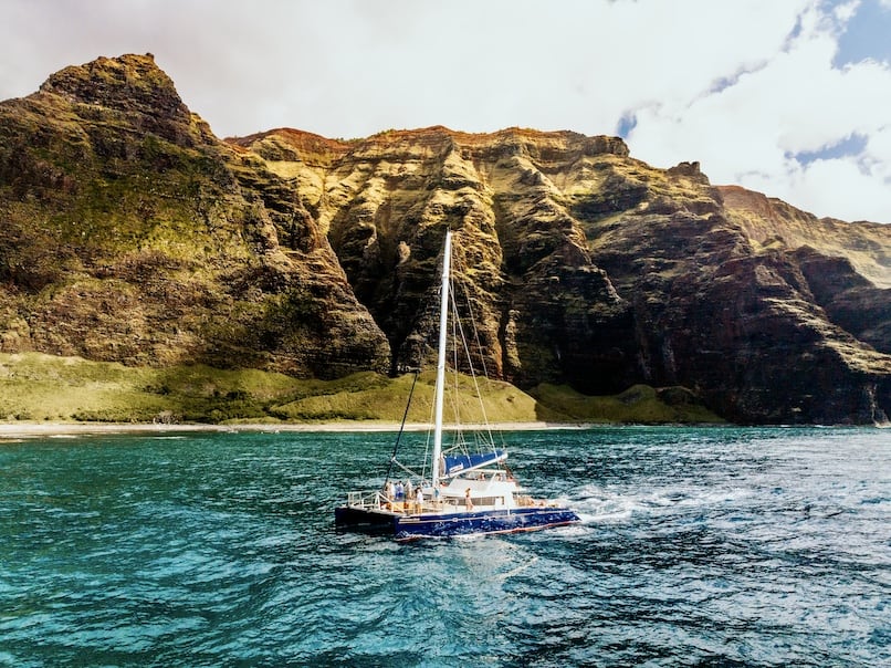 Captain Andy's catamaran sailing along the Na Pali Coast, with towering cliffs in the background and clear blue ocean water.