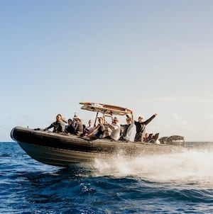 A group of people enjoying a high-speed boat ride on the ocean, with water spraying and a clear sky in the background.