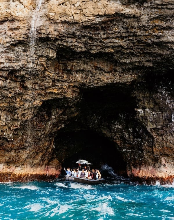 Boat entering a dramatic sea cave along the Na Pali Coast, surrounded by rugged cliffs and turquoise ocean water.