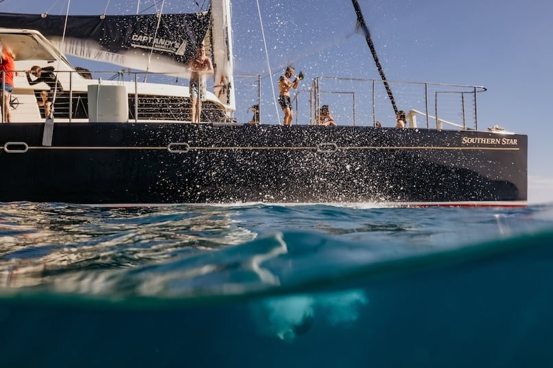 Guests jumping off Captain Andy's catamaran, Southern Star, into the clear blue ocean, with water splashing and the boat visible in the background.