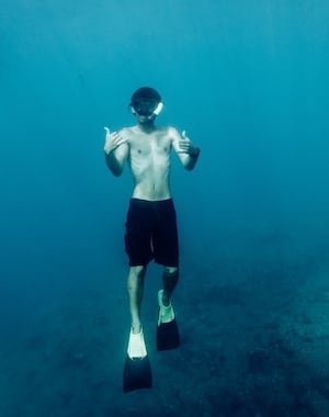 A snorkeler underwater near the Na Pali Coast, making shaka signs while wearing fins and a mask in the clear blue ocean