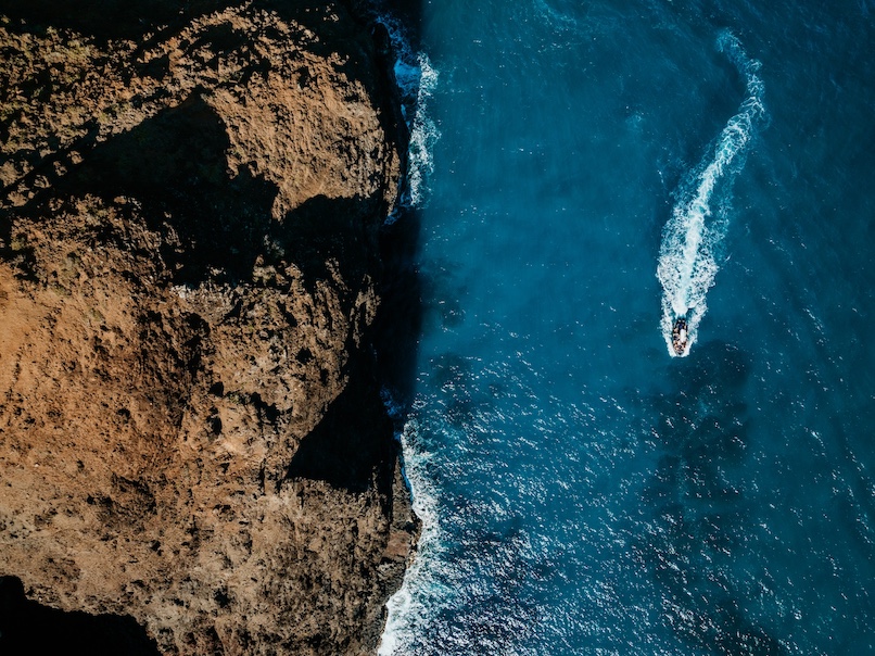Aerial view of a boat speeding along the rugged coastline of the Na Pali Coast.