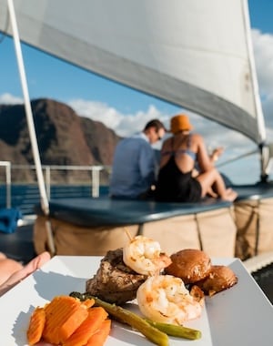 Gourmet meal served on a plate with a couple sitting on a boat deck in the background.
