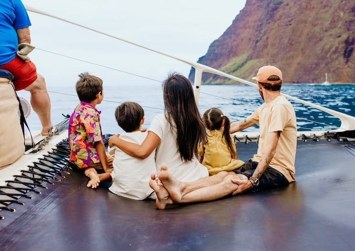 Family sitting on a Captain Andy's catamaran, enjoying the view of the Na Pali Coast with its steep cliffs and blue ocean water.